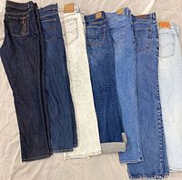 Seven pairs of women’s jeans laid flat side-by-side showing color range and waistband patches