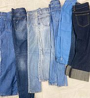 Seven pairs of assorted women’s jeans laid flat showing color variety and styles