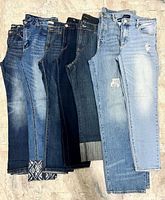 Seven pairs of jeans laid side by side showing front legs and varying washes