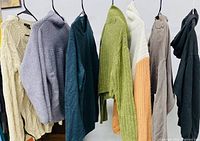 Seven assorted women’s medium sweaters hanging side by side