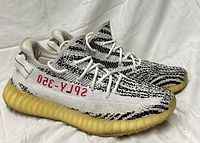 Lateral view of both sneakers showing side profile, Primeknit pattern, red text, yellowed midsole