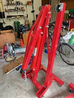 Folded red steel engine hoist with casters, boom, jack and hook visible