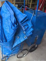 Folded blue tarps in wire-frame trolley next to blue metal box trolley