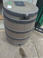 Full view of brown plastic rain barrel showing spigot and leak