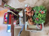Box and bin showing ornaments, wrapping paper, wreath, plush gingerbread, ribbons