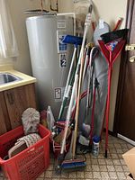 Group view showing ironing board, brooms, mop, duster, baskets, steamer, iron, starch