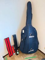 Upright bass inside navy padded gig bag with two hard bow cases beside it