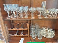 Cabinet shelf with assorted stemware, highball tumblers, lowball glasses, wooden wine rack, metal tray