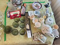 Overall view showing teapot, green glasses, vase, boxed flatware, coasters, decorative plates, candlesticks
