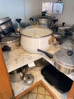 Cabinet shelf showing multiple stainless pans, white enamel stock pot, lower shelf items