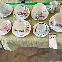 All seven cup and saucer sets with creamer and extra saucers displayed on table