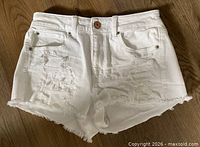 Front view of white distressed cutoff shorts showing rips and frayed hem