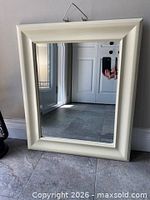 Front view of cream framed beveled mirror resting on floor