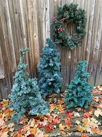 All three faux trees and wreath displayed against fence