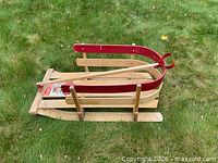 Side view of the wooden sleigh showing red siderails, pull handle, runners and seat