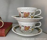 Stacked teacups on saucers showing floral design and scalloped rims