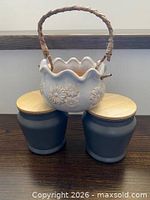 Two grey ceramic jars with wood lids and white planter with rattan handle