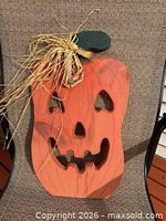 Front view of wooden pumpkin showing carved facial features and raffia bow