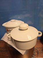 Two covered casserole dishes, one fruit pattern, one plain white