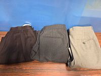 Three folded pairs of dress pants in brown, grey and beige on tabletop