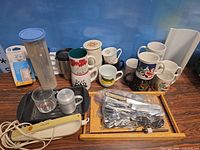 Overview of lot showing mugs, Philips appliance, plastic container, safety plug covers, flatware bag, tray