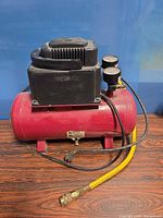 Full view of red air compressor with yellow hose on wood floor