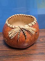 Side view of dried gourd vase showing raffia-stitched rim and tassel with beads