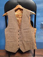 Front view of brown tweed vest on hanger showing pockets and buttons