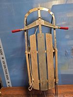 Full view of vintage steerable wooden sled with red hand grips and pull rope
