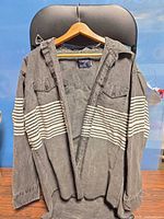 Front view of Wrangler charcoal grey jacket with white horizontal stripes, hung on hanger