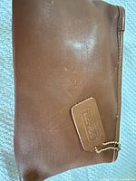 Front of tan Coach leather pouch showing hangtag and embossed logo