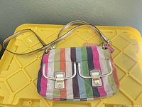 Front view of Coach multicolor striped shoulder bag on yellow surface