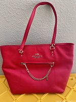 Front view of red Coach Saffiano leather tote showing gold-tone hardware, zipper pocket, chain detail and shoulder straps
