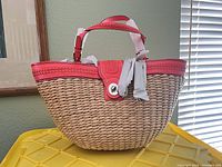 Front/side view of Coach woven raffia tote showing coral leather trim, handles, turn lock tab and overall shape