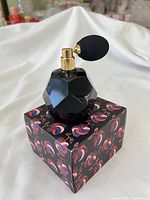 Faceted black perfume bottle with gold spray and atomizer bulb sitting on patterned Diptyque box