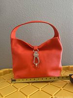 Front view of orange leather shoulder bag with measuring tape
