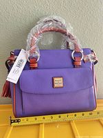Front view of purple Dooney & Bourke satchel with tag attached, handle wrapped, tape measure indicates width