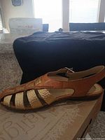 Side profile of Jeepers gold and tan leather slingback sandal on top of original box