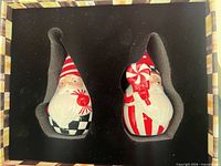 Two Santa shakers seated in custom foam inside decorative box