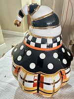 Full view of cookie jar with lid showing checkered collar, polka dot ruffle, plaid body, gold accents and twisted finial