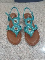 Full pair of teal leather Reba sandals on granite surface
