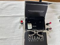 Open presentation box showing interior velvet insert, rhinestone bow clasp, three lipstick-style atomizers, and silica packet