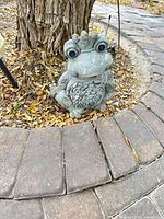 Front view of gray frog statue positioned in garden setting