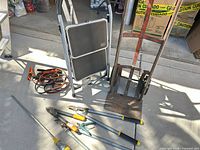 Overview of hand truck, step stool, ladder edge, tools on ground