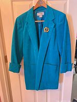 Full view of teal Ultrasuede blazer on hanger with brooch attached