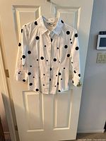Full front view of white shirt with black polka dots on hanger