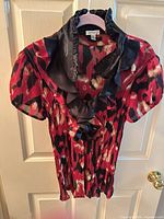 Full view of crepe blouse on hanger showing print, sleeves and ruffled collar