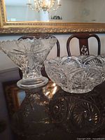 Two clear cut glass bowls on table: pedestal compote left, scalloped bowl right