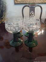Four cordial glasses on table showing green stems and etched bowls