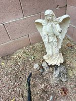 Full view of angel statue against brick wall showing overall condition